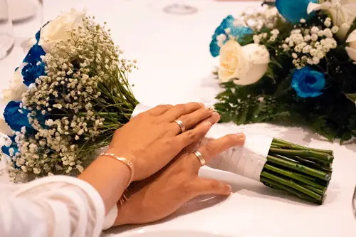 Manos de los novios con anillos sobre la mesa y ramos de flores