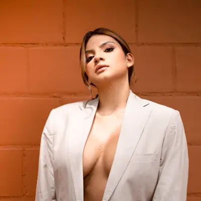 Mujer con blazer claro posando frente a pared de ladrillo