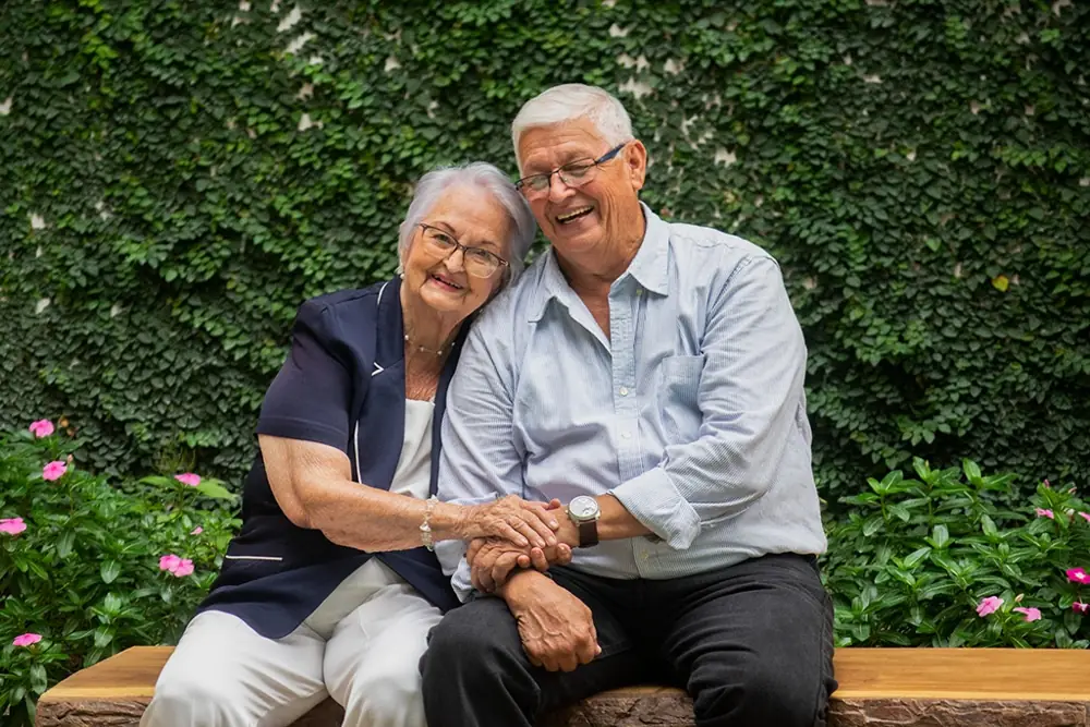 Pareja de adultos mayores sonriendo abrazados en un jardín